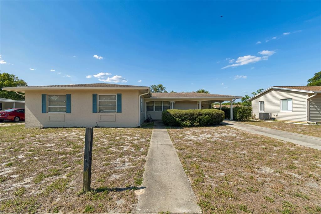 A single-story house with a beige stucco exterior, blue shutters, and a front carport — 6432 SPRING HILL DRIVE, SPRING HILL, FL