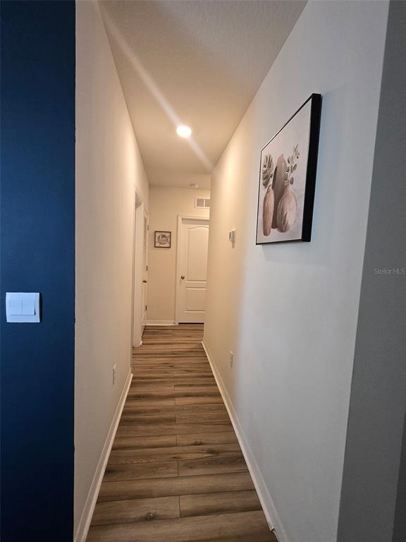 A hallway with wood-look flooring, a dark blue accent wall, and framed wall art — 1760 CARNOSTIE ROAD, WINTER HAVEN, FL
