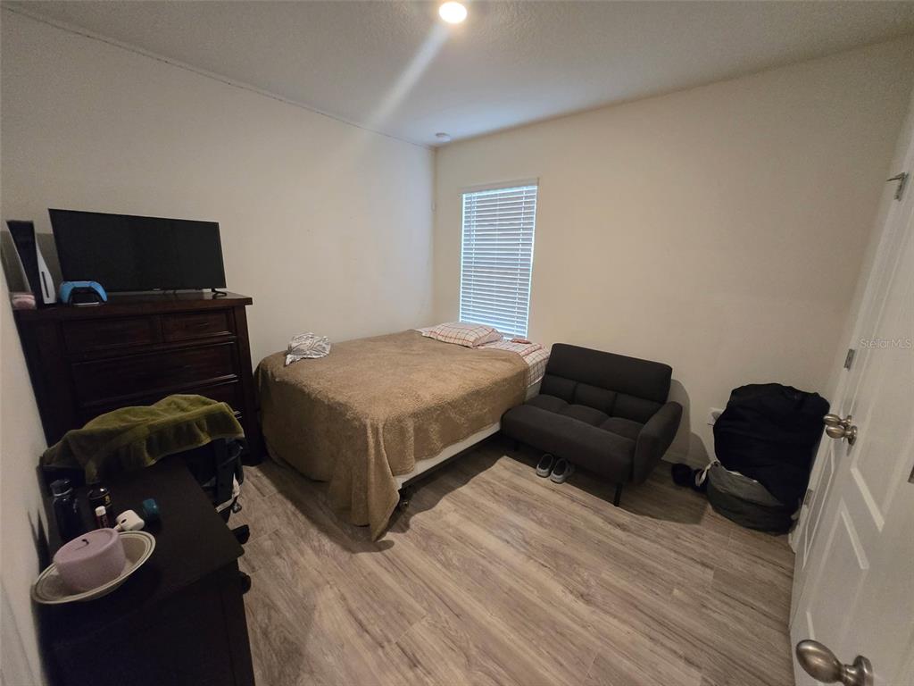 A bedroom features a bed, a dark sofa, a dresser with a television, and wood-look flooring — 1760 CARNOSTIE ROAD, WINTER HAVEN, FL