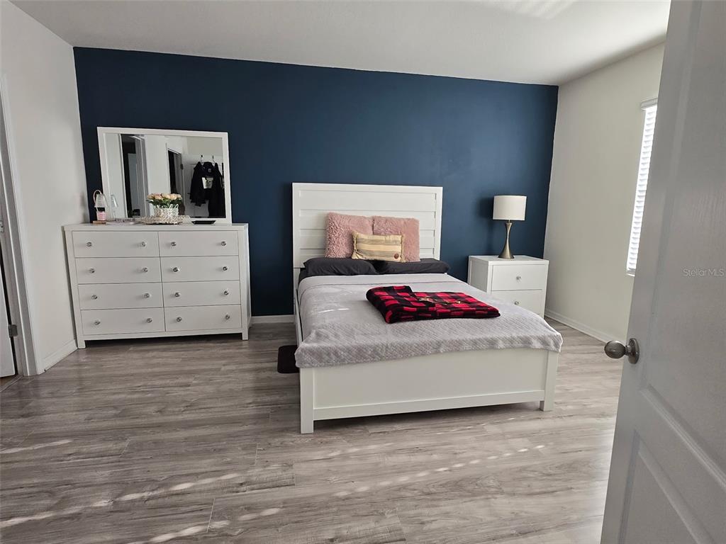 A bedroom features a navy accent wall, white furniture, and light wood-look flooring — 1760 CARNOSTIE ROAD, WINTER HAVEN, FL