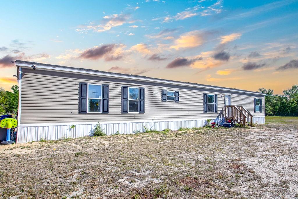 A long, single-story manufactured home with gray siding sits on a sandy, open lot — 1147 SE HAMMERLY STREET, MADISON, FL