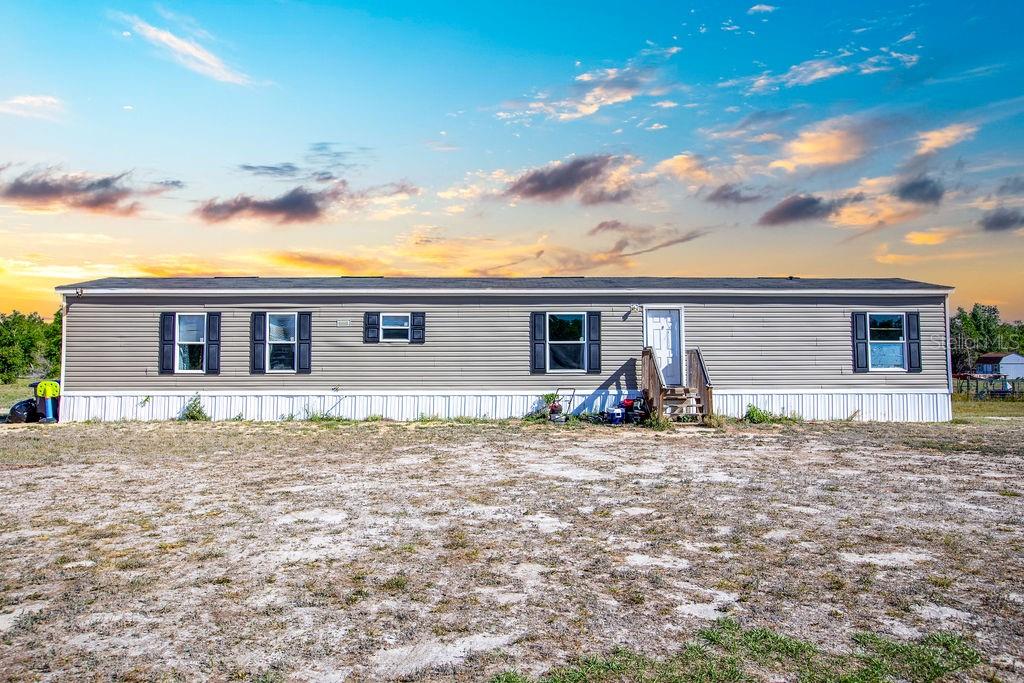 A single-story manufactured home with gray siding sits on a large, dry dirt lot — 1147 SE HAMMERLY STREET, MADISON, FL