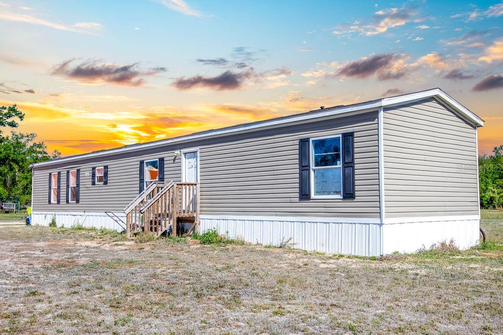 A single-story manufactured home with grey siding and white skirting sits on a dirt lot — 1147 SE HAMMERLY STREET, MADISON, FL