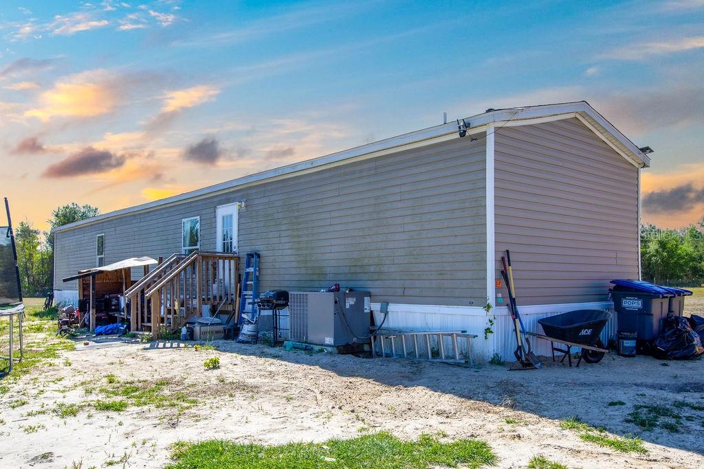 The exterior of a tan manufactured home features a wooden staircase and a sandy yard — 1147 SE HAMMERLY STREET, MADISON, FL