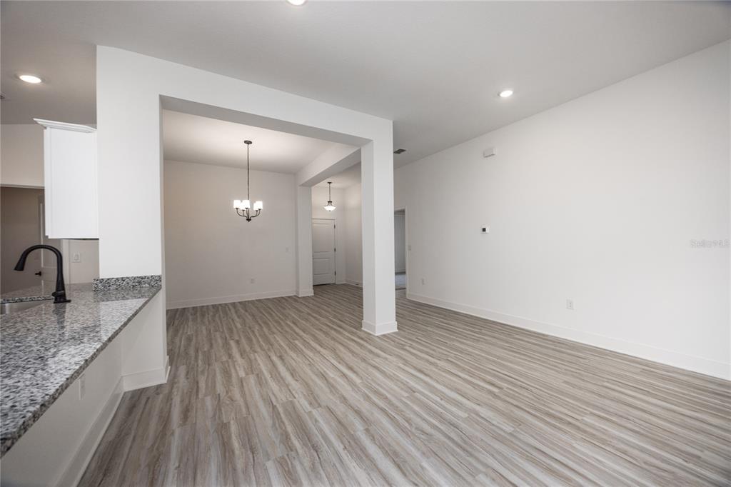An open-concept dining area features light wood-look flooring, white walls, and a granite kitchen counter — 2573 SW 250TH DRIVE, NEWBERRY, FL
