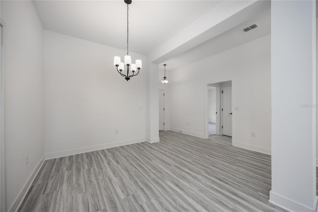 An empty dining area features white walls, gray wood-look flooring, and two hanging light fixtures — 2573 SW 250TH DRIVE, NEWBERRY, FL