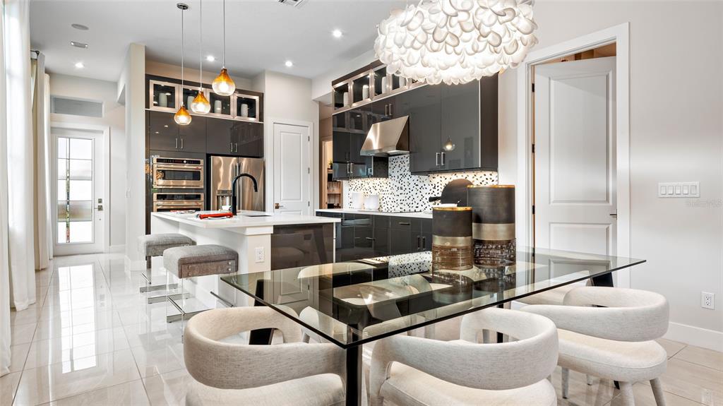 A modern kitchen features dark cabinetry, a glass dining table, and white tile flooring — 1580 BELLAGIO LOOP, TAVARES, FL