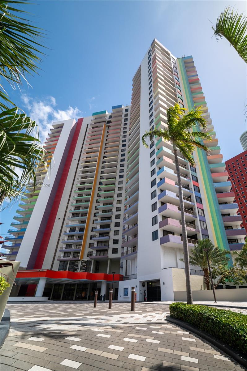 A tall, multi-colored apartment building stands above a paved courtyard with palm trees — 1581 Brickell Ave, Miami FL 33129, MIAMI, FL