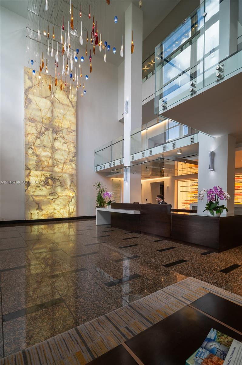 A modern building lobby features a tall illuminated stone wall, glass railings, and a reception desk — 1581 Brickell Ave, Miami FL 33129, MIAMI, FL
