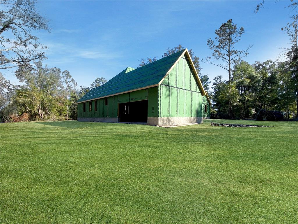 A partially constructed building with green sheathing stands in a large, grassy field — 5783 NE 51ST TERRACE, HIGH SPRINGS, FL