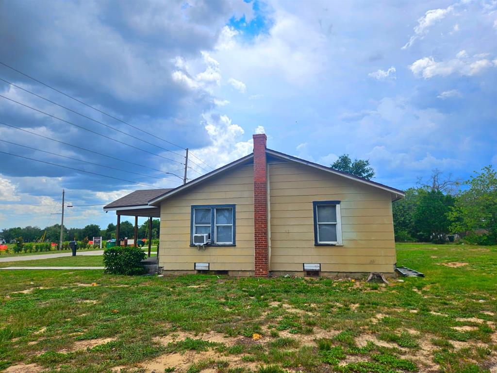The exterior side view of a tan, single-story house features a brick chimney and windows — 507 FLORIDA AVENUE, DUNDEE, FL