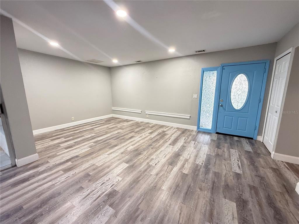 An empty room features gray walls, wood-look flooring, a blue front door, and recessed lighting — 7 CHIP COURT, KISSIMMEE, FL