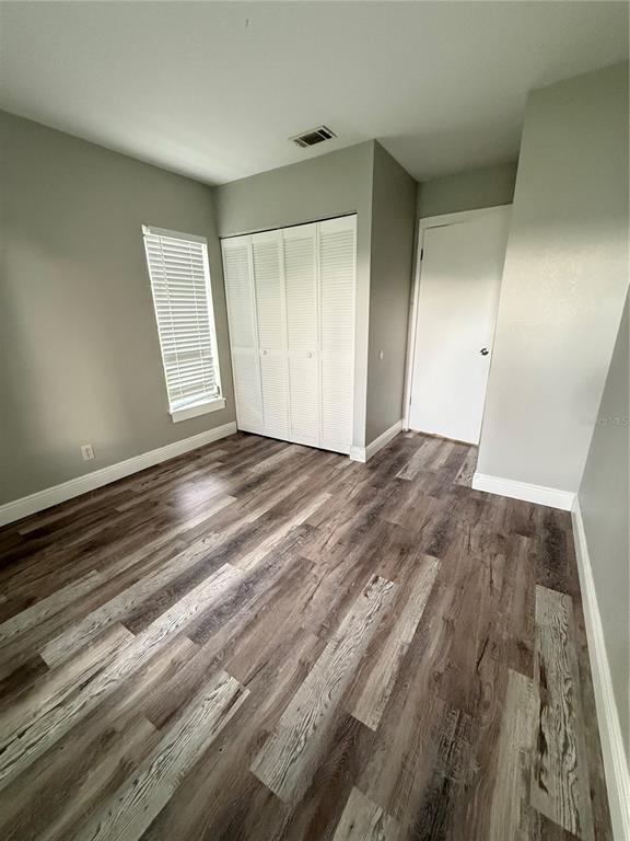 An empty bedroom features light gray walls, wood-look flooring, a window, and white closet doors — 7 CHIP COURT, KISSIMMEE, FL