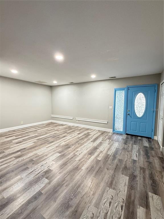 An empty room with wood-look flooring, light gray walls, and a bright blue front door — 7 CHIP COURT, KISSIMMEE, FL