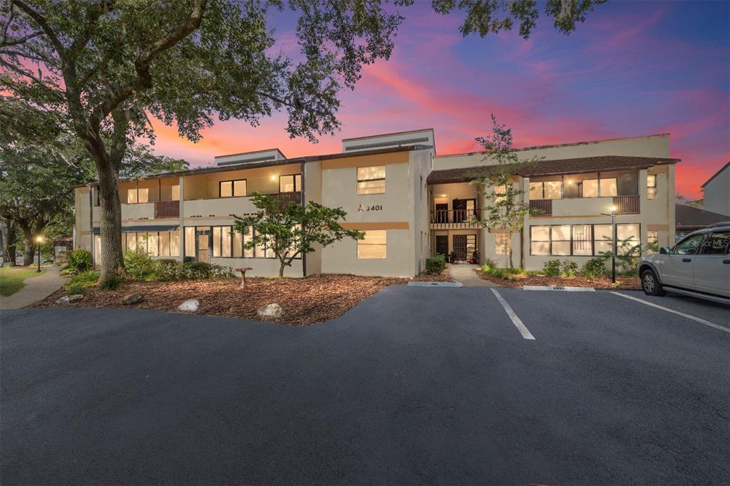 A three-story apartment building exterior with a parking lot and large tree at sunset — 3401 E FORT KING STREET UNIT 202, OCALA, FL