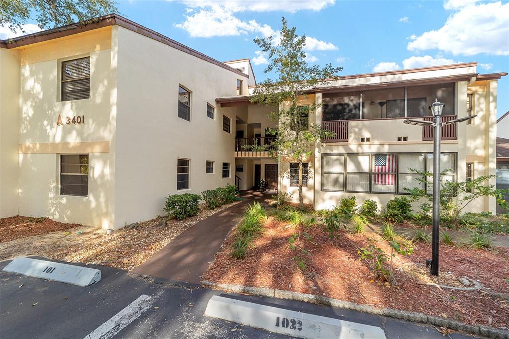A two-story apartment building exterior features tan stucco walls, a walkway, and parking spaces — 3401 E FORT KING STREET UNIT 202, OCALA, FL