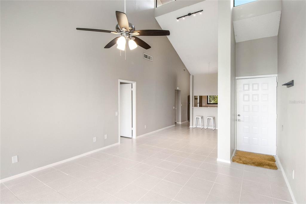 A bright, open-concept living area features vaulted ceilings, a ceiling fan, and light tile flooring — 410 LAUREL COVE WAY, WINTER HAVEN, FL
