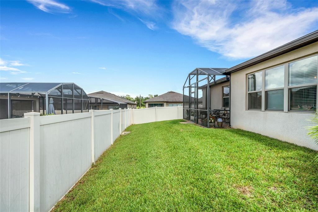 A grassy backyard features a white vinyl fence and a screened-in patio attached to a house — 519 VIGO STREET, DAVENPORT, FL