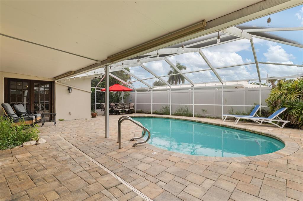 A covered patio with pavers overlooks a swimming pool enclosed by a screen cage — 8404 FLAGSTONE DRIVE, TAMPA, FL