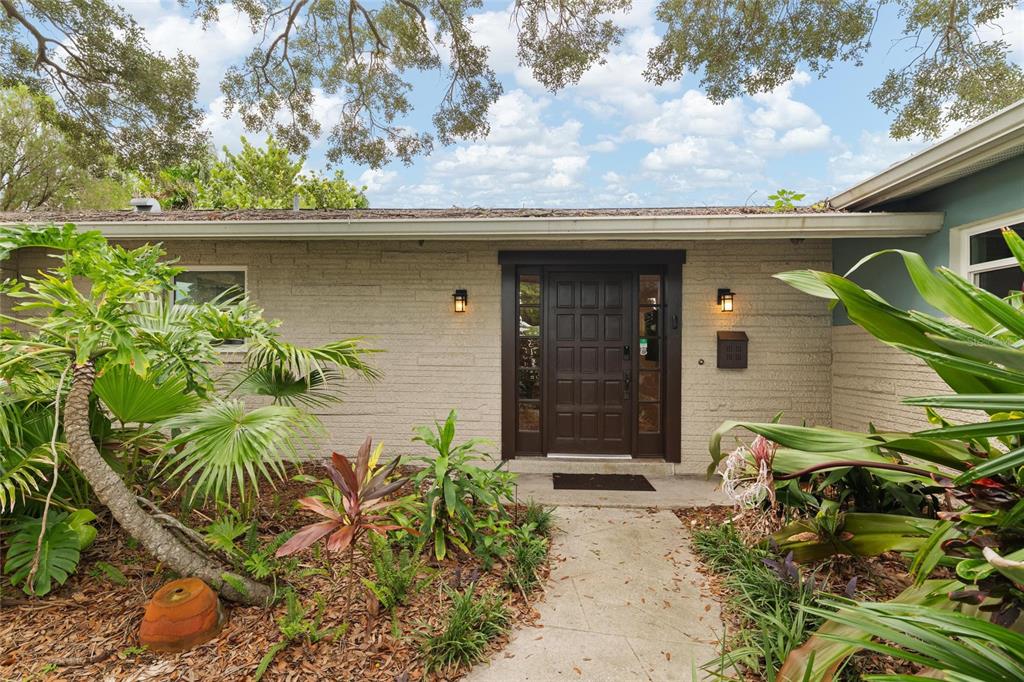 The exterior of a single-story house features a brown front door, stone siding, and landscaping — 8404 FLAGSTONE DRIVE, TAMPA, FL