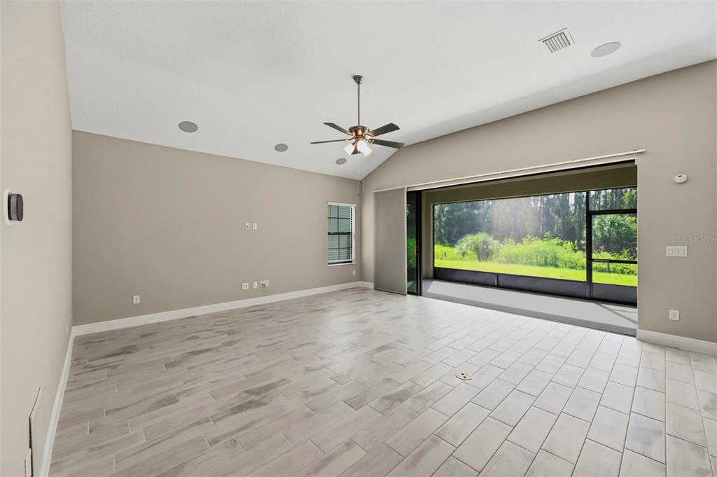 A spacious living room features light tile flooring, a vaulted ceiling, and large sliding glass doors — 14519 WOODLAND SPUR DRIVE, LITHIA, FL