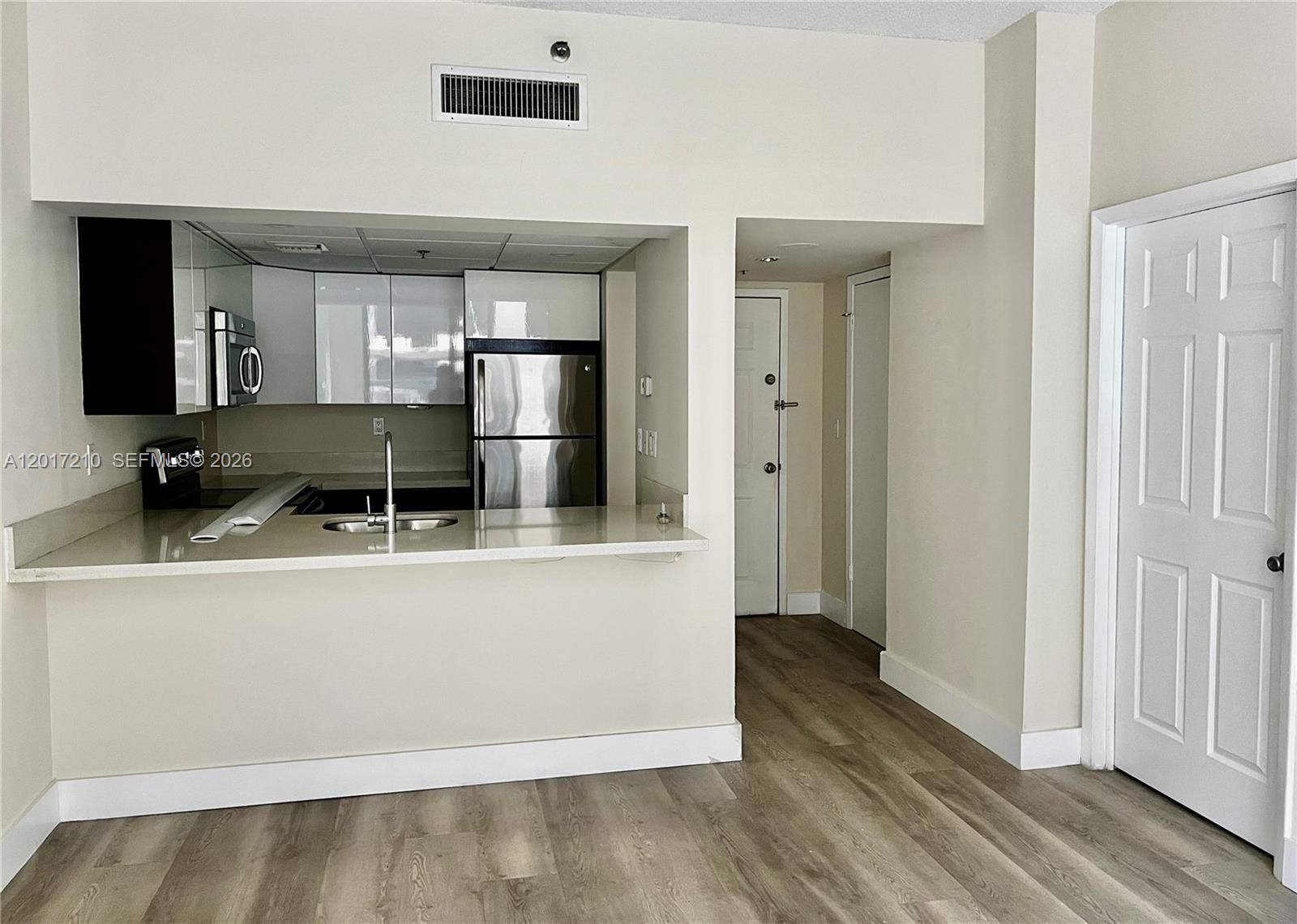 A kitchen with stainless steel appliances and a breakfast bar overlooks a wood-floored hallway — 540 Brickell Key Dr # 218, Miami FL 33131, MIAMI, FL