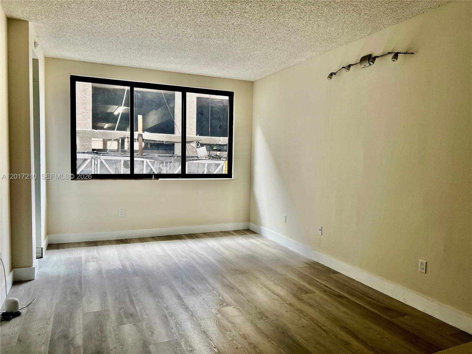 An empty room features wood-look flooring, a popcorn ceiling, and a large window — 540 Brickell Key Dr # 218, Miami FL 33131, MIAMI, FL