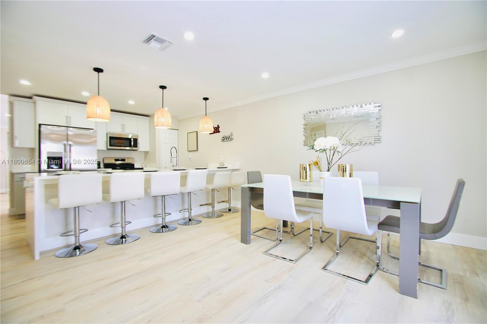 A modern kitchen and dining area featuring white cabinetry, a breakfast bar, and contemporary furniture — 244 NW 6th Ave # 244, Delray Beach FL 33444, DELRAY BEACH, FL