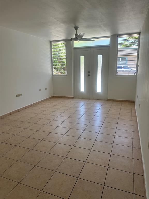 An empty room with beige tile flooring, a ceiling fan, and double glass-paneled doors — 2821 CALLE 13, RINCON, PR
