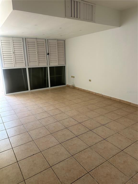 An empty room features beige tile flooring, white walls, and a wall of shuttered windows — 2821 CALLE 13, RINCON, PR