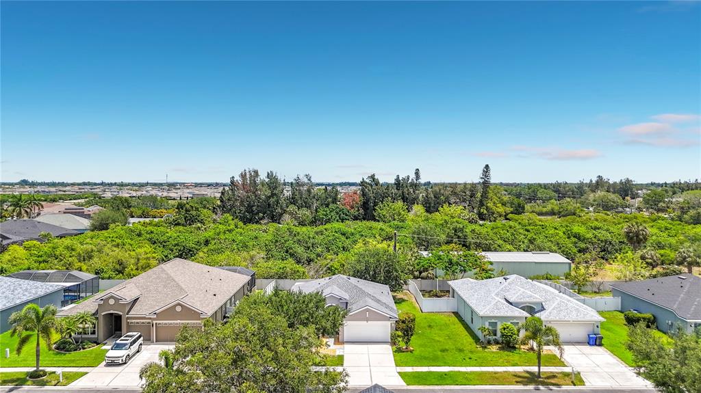 An aerial view shows three suburban houses with driveways and lawns bordering a wooded area — 1810 BONITA BLUFF COURT, RUSKIN, FL