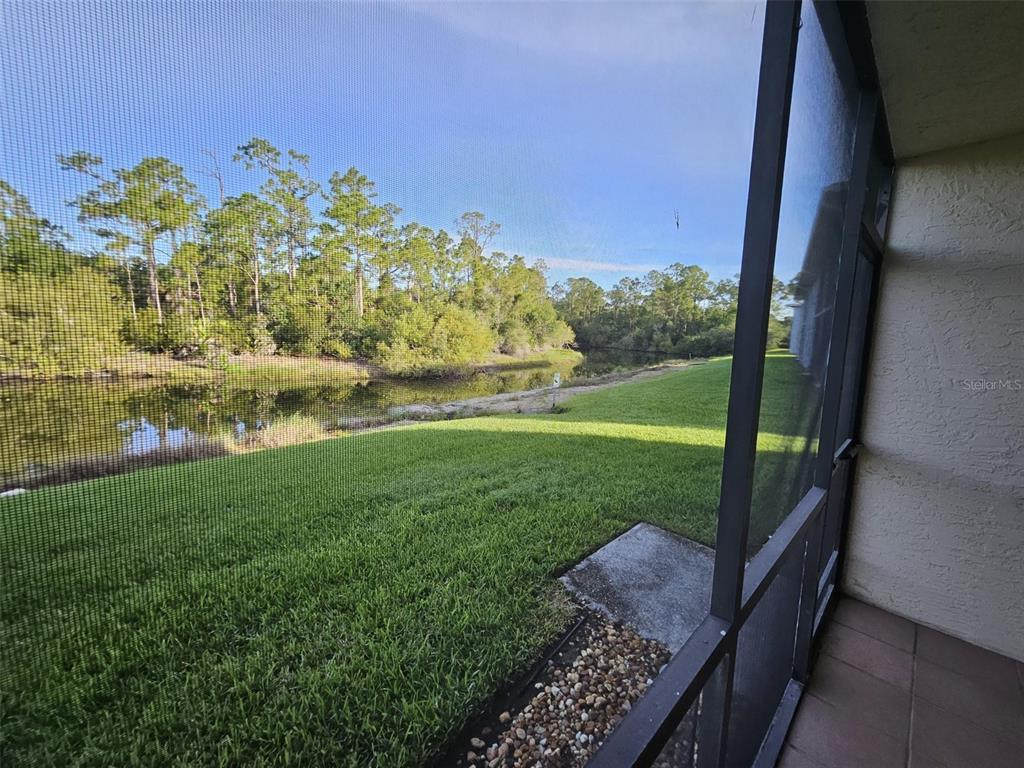 A view of a grassy backyard and a pond through a screened-in patio enclosure — 25050 SANDHILL BOULEVARD UNIT 5A4, PUNTA GORDA, FL