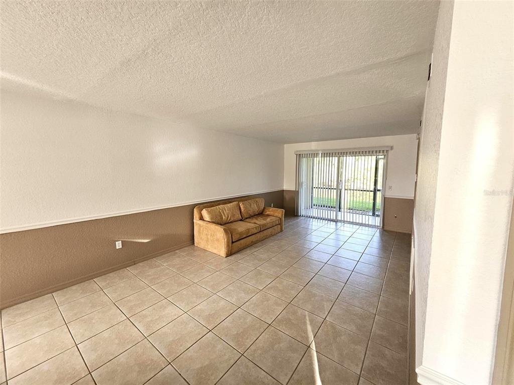 A living room features beige tile flooring, two-toned walls, and a tan sofa near sliding doors — 25050 SANDHILL BOULEVARD UNIT 5A4, PUNTA GORDA, FL