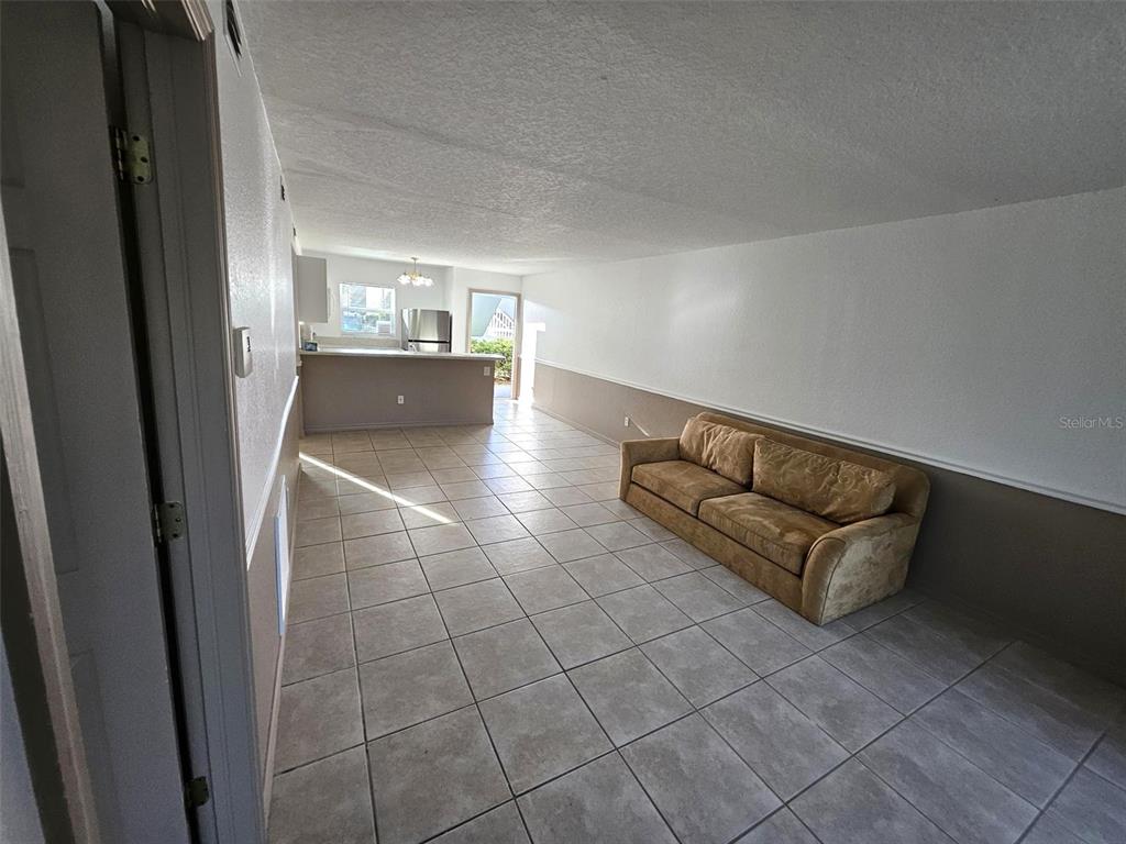 A living room with tile flooring and a tan sofa leads to an open kitchen — 25050 SANDHILL BOULEVARD UNIT 5A4, PUNTA GORDA, FL