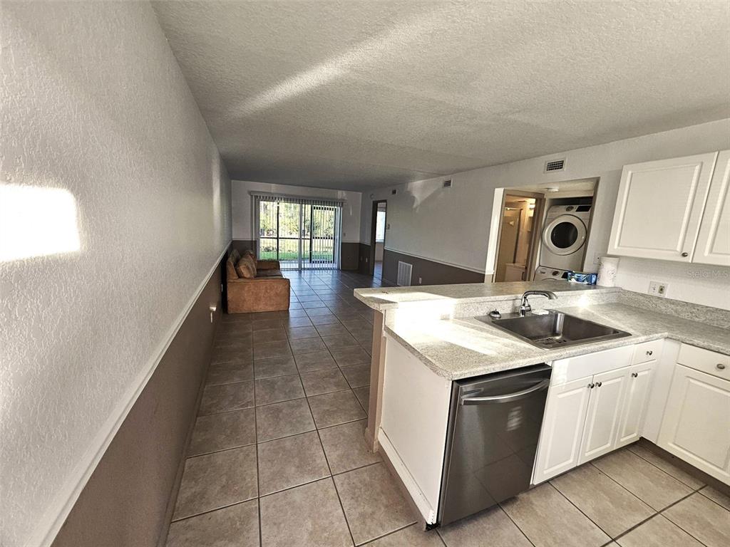 A kitchen with white cabinets and stainless steel appliances overlooks a living area with tile — 25050 SANDHILL BOULEVARD UNIT 5A4, PUNTA GORDA, FL