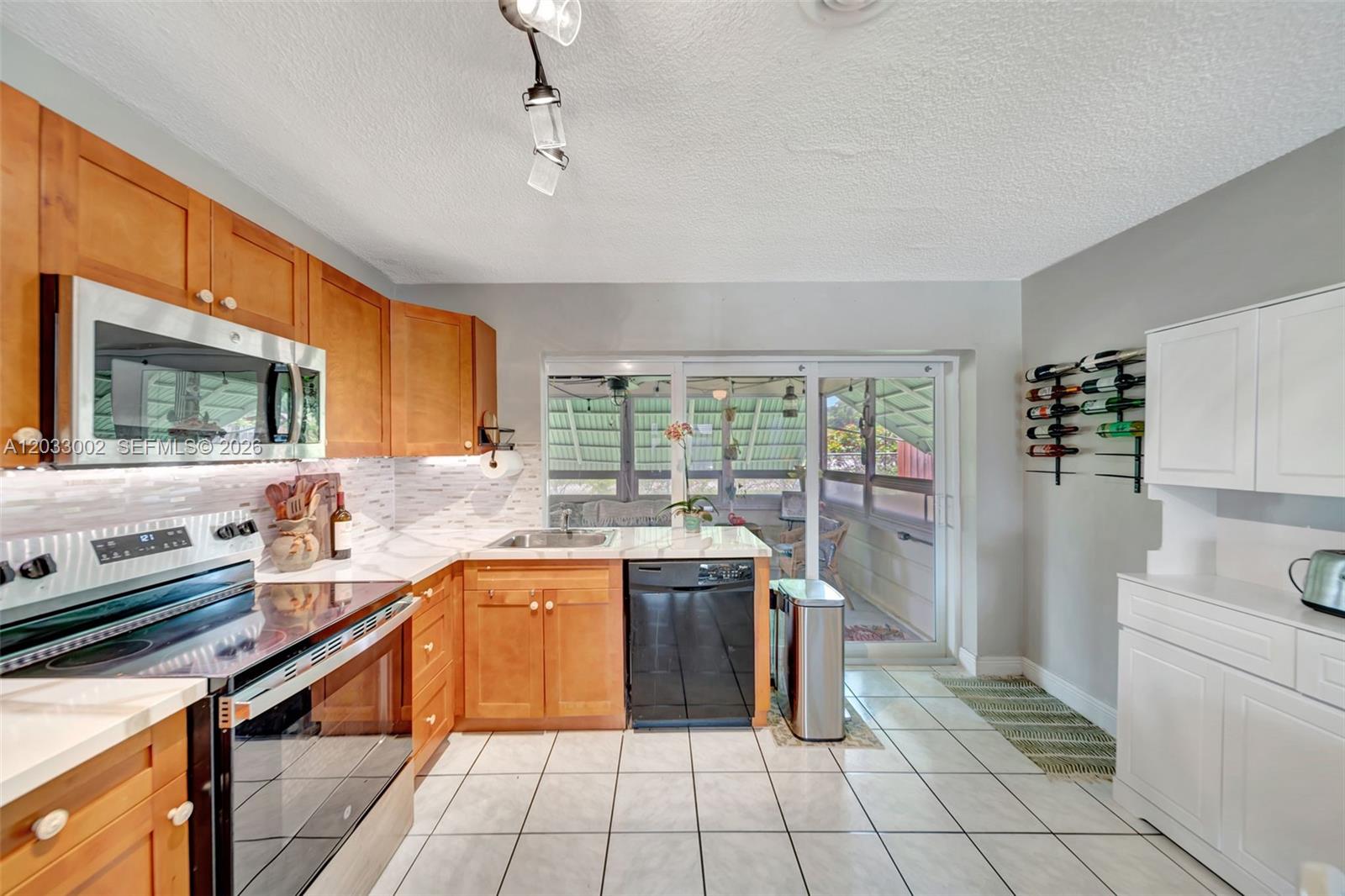 A kitchen features wood cabinets, stainless steel appliances, white tile floors, and a sliding door — 2708 NW 51st Pl, Tamarac FL 33309, TAMARAC, FL
