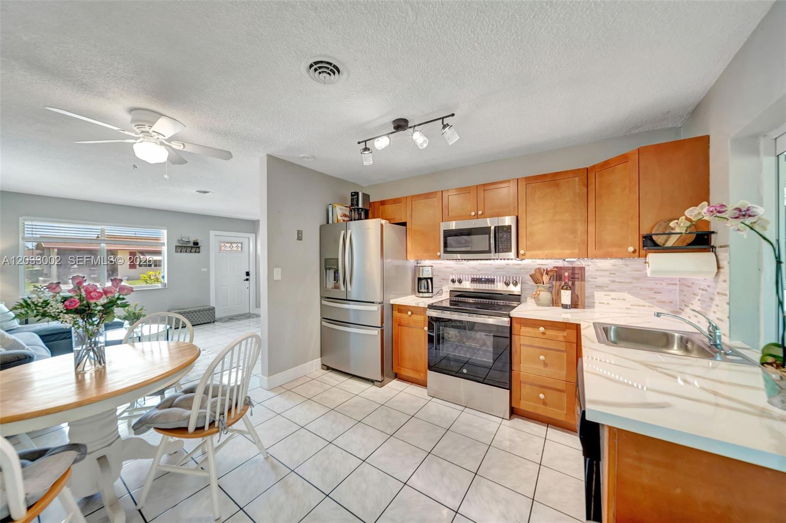 A kitchen features wood cabinets, stainless steel appliances, and a dining area with white chairs — 2708 NW 51st Pl, Tamarac FL 33309, TAMARAC, FL