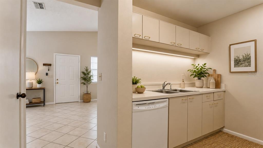 A kitchen area with white cabinets and a dishwasher overlooks a tiled entryway and door — 3848 59TH AVENUE W, BRADENTON, FL