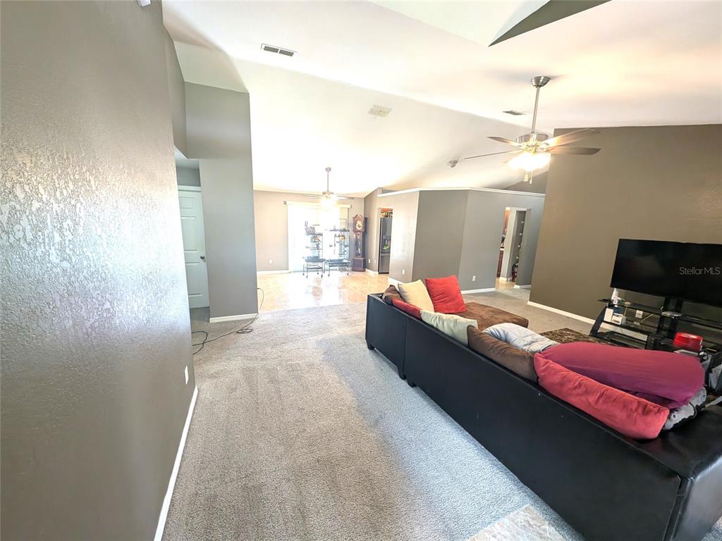 A living room features gray walls, carpeted flooring, a sectional sofa, and vaulted ceilings — 14968 SW 25TH CIRCLE, OCALA, FL