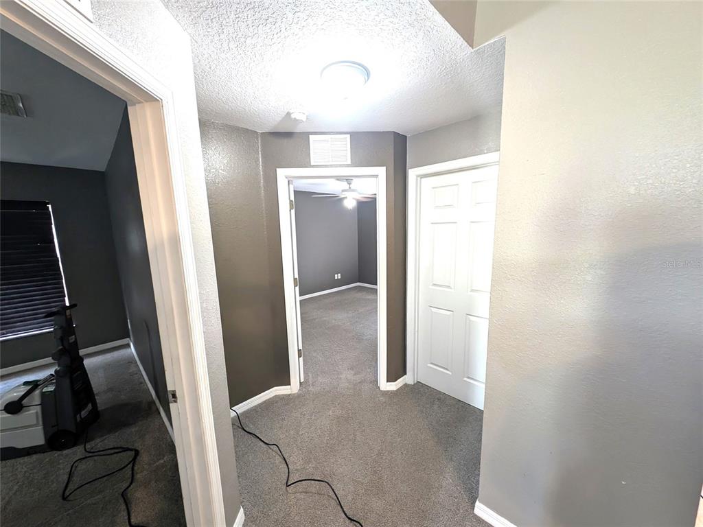 A hallway with gray walls and carpet leads to a bedroom with a ceiling fan — 14968 SW 25TH CIRCLE, OCALA, FL