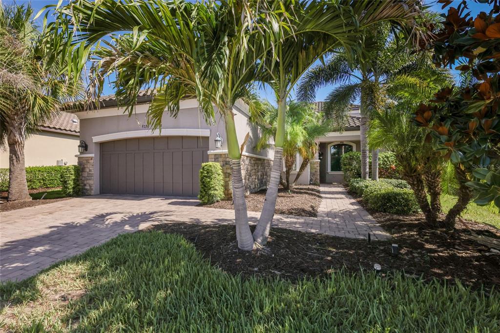 A single-story house with a two-car garage, stone accents, and palm trees in the front — 9728 HIGHLAND PARK PLACE, PALMETTO, FL