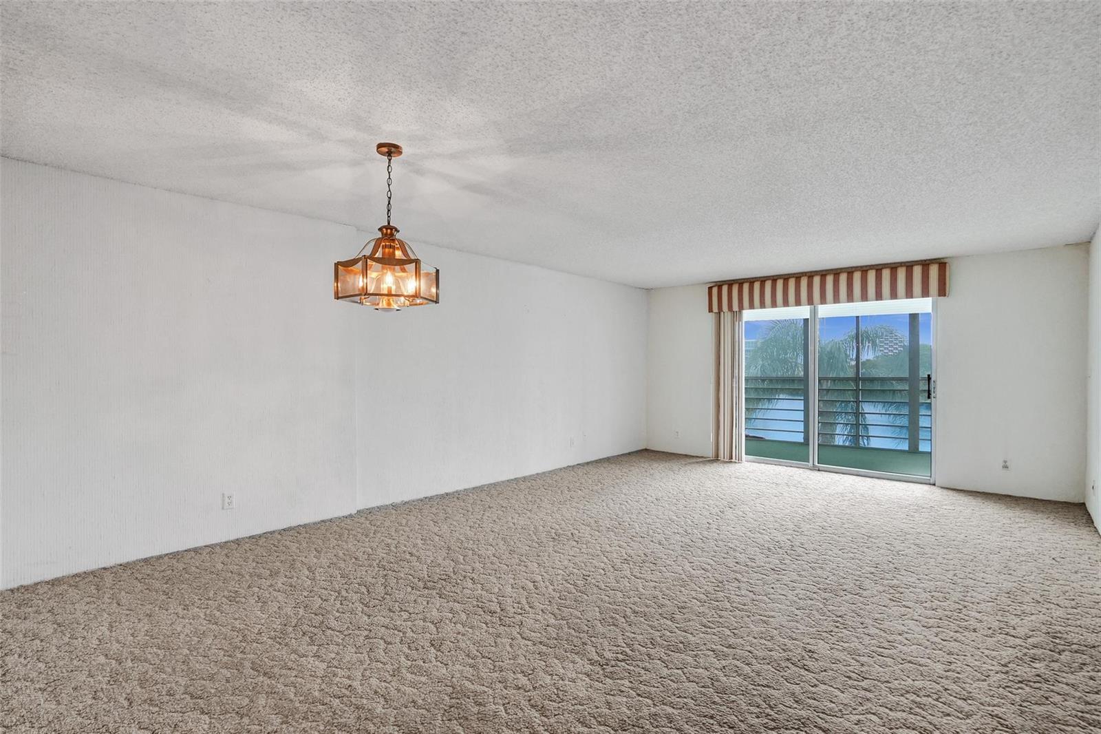 An empty living room with beige carpet, white walls, a hanging light fixture, and sliding doors — 131 SE 3rd Avenue # 304, Dania Beach FL 33004, DANIA BEACH, FL