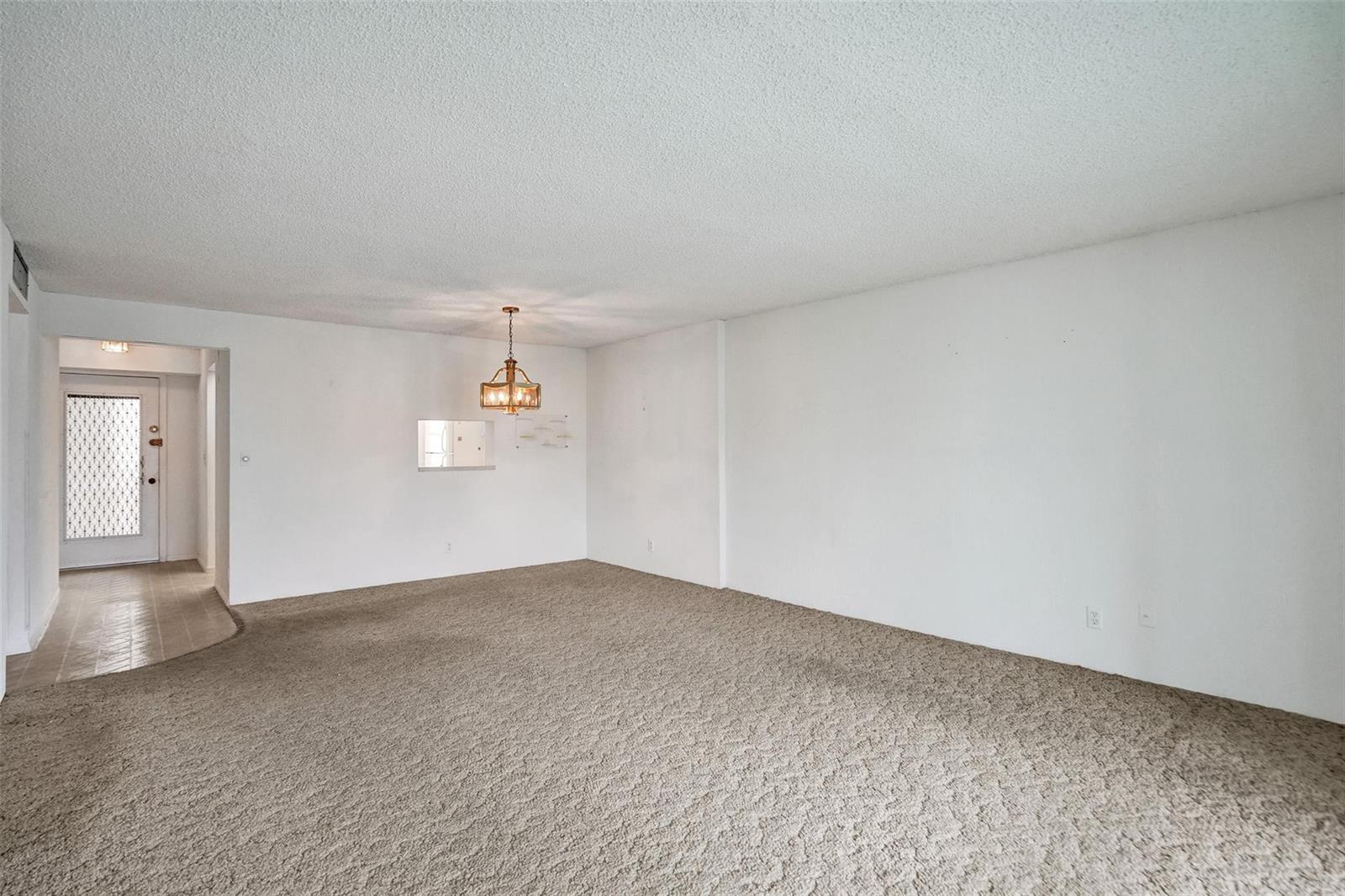 An empty living room features beige wall-to-wall carpeting, white walls, and a hanging light fixture — 131 SE 3rd Avenue # 304, Dania Beach FL 33004, DANIA BEACH, FL