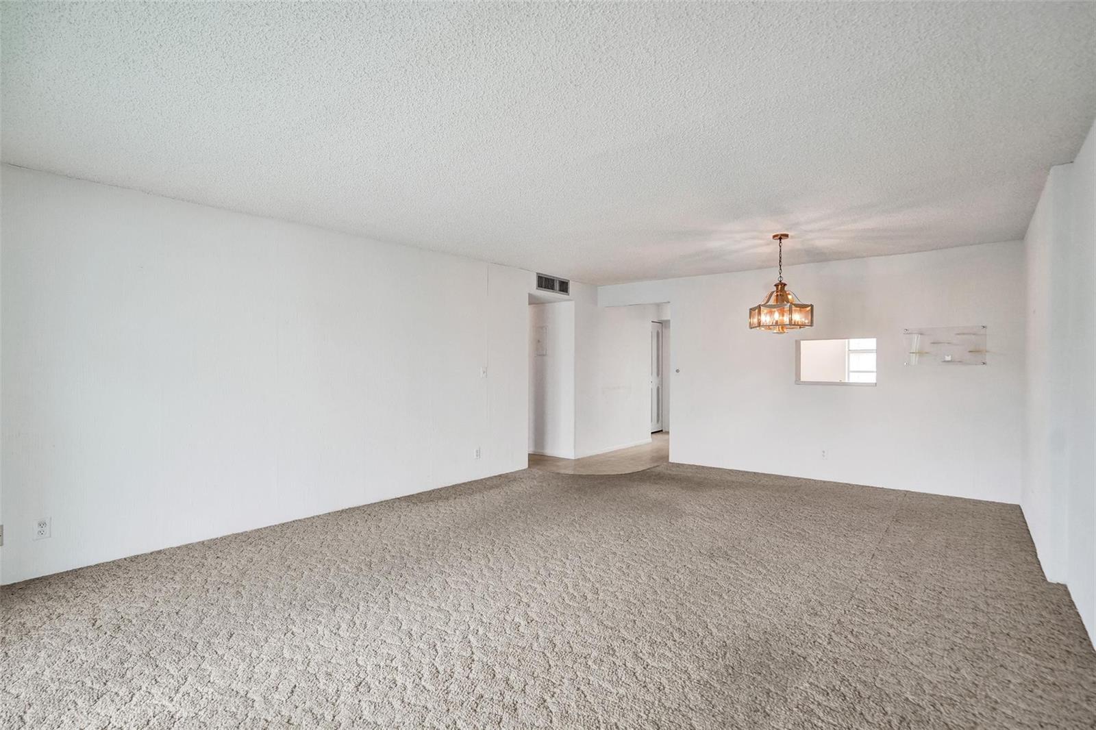 An empty room with beige carpet, white walls, a popcorn ceiling, and a hanging chandelier — 131 SE 3rd Avenue # 304, Dania Beach FL 33004, DANIA BEACH, FL