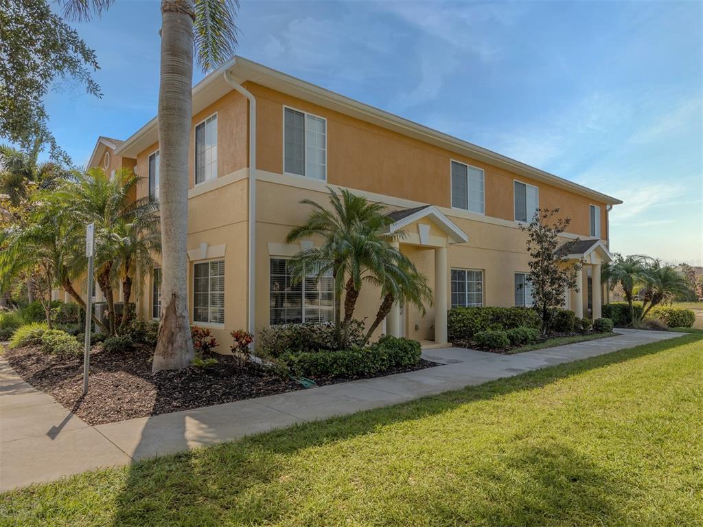 A two-story tan apartment building features palm trees and a sidewalk along the front exterior — 12905 TIGERS EYE DRIVE, VENICE, FL