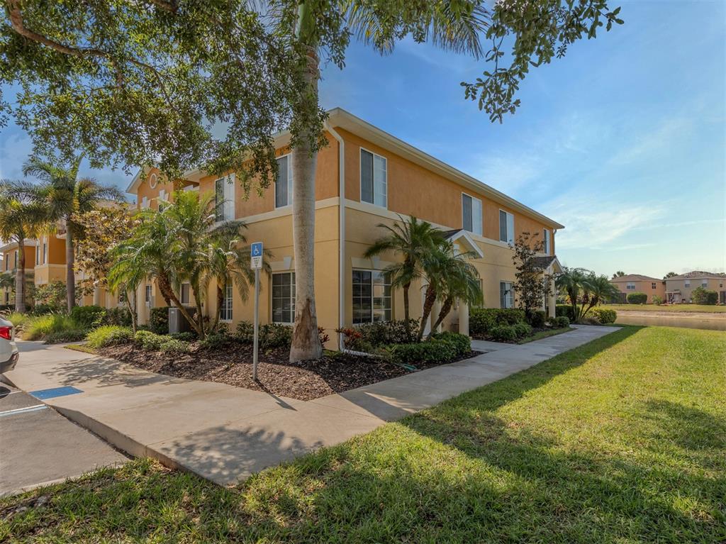 A two-story tan apartment building with palm trees and a sidewalk on a sunny day — 12905 TIGERS EYE DRIVE, VENICE, FL