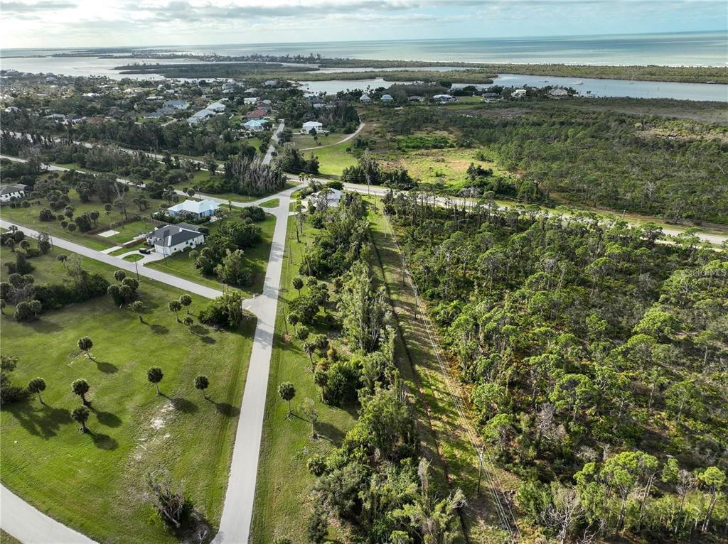 An aerial view shows a paved road winding through a grassy, wooded coastal residential area — 70 COBIA DRIVE, PLACIDA, FL