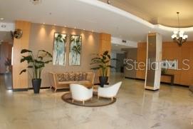A lobby area features a sofa, two white chairs, potted plants, and light-colored tile flooring — 880 MANDALAY AVENUE UNIT S404, CLEARWATER, FL