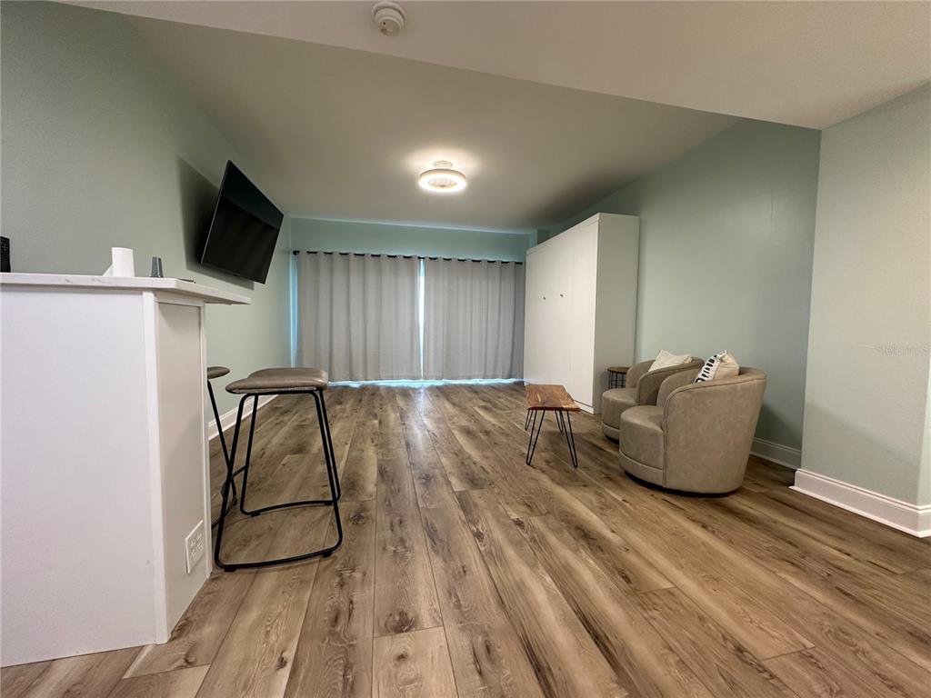 A living room features wood-look flooring, a breakfast bar, two armchairs, and a wall bed — 880 MANDALAY AVENUE UNIT S404, CLEARWATER, FL