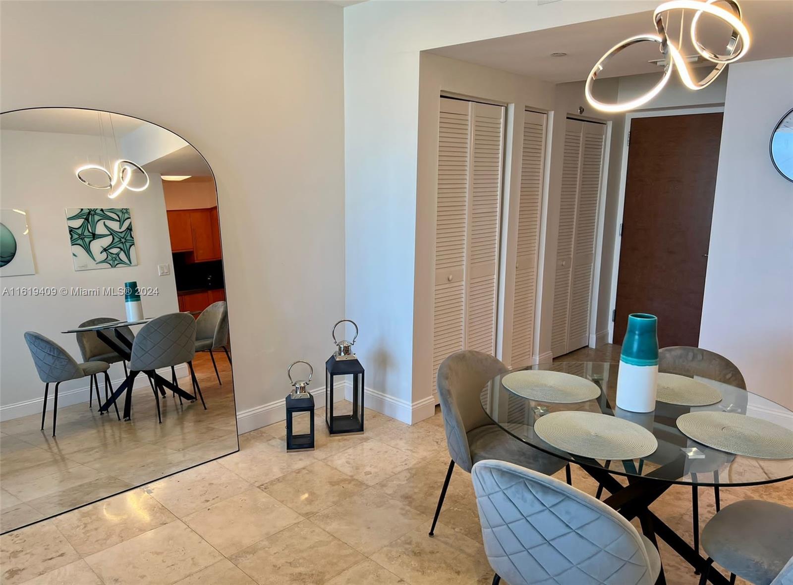 A dining area features a glass table, grey chairs, a large arched mirror, and tile flooring — 6365 Collins Ave # 2610, Miami Beach FL 33141, MIAMI BEACH, FL